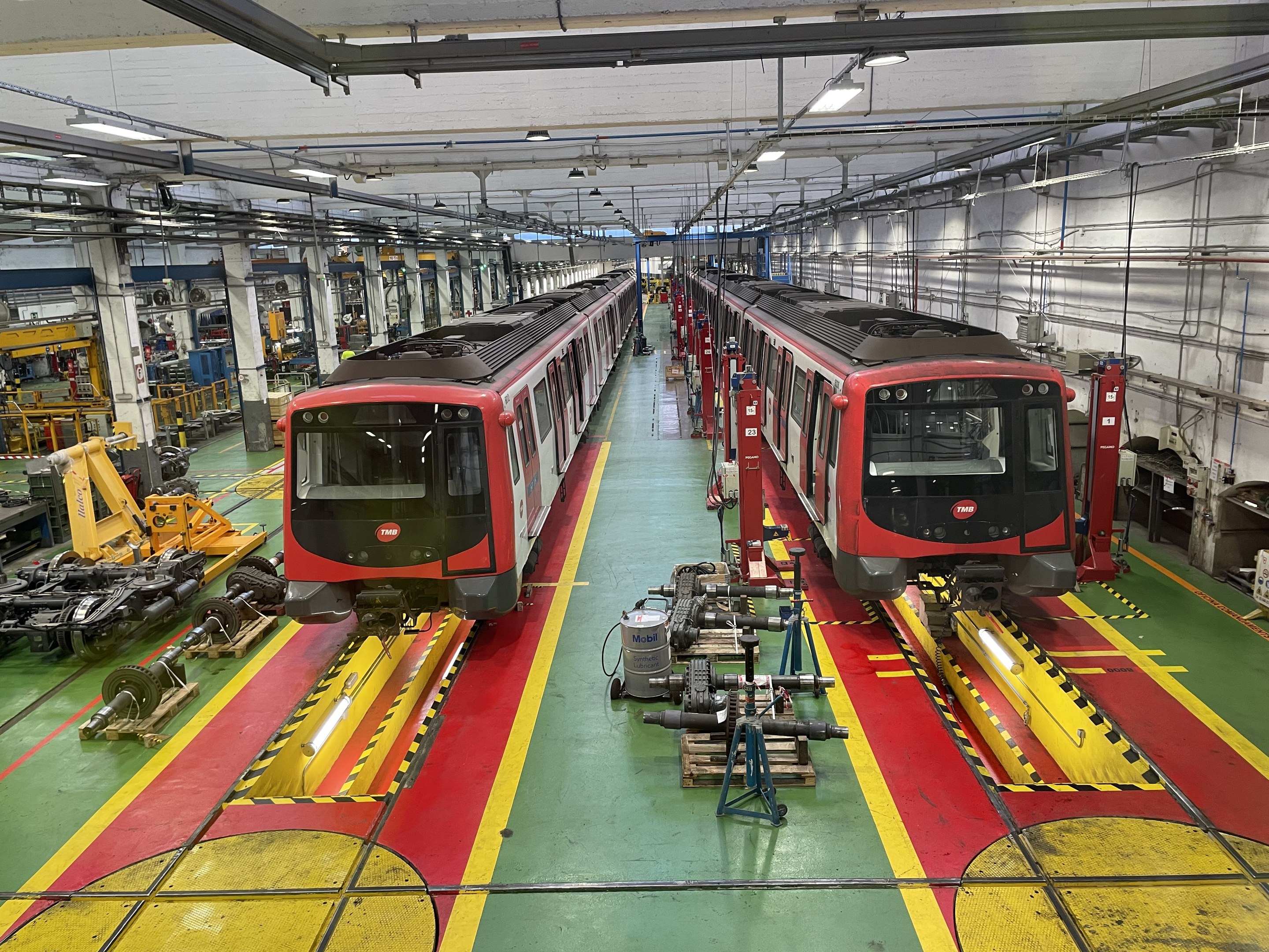 Zwei Züge auf den Schienen in einer Daimler Group Fabrik mit Maschinen und Rohren an der rechten Wand.