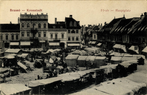 Schwarz-weiß-Foto eines belebten Marktes in Kronstadt, Deutschland, mit Menschen, Zelten und Gebäuden unter einem sichtbaren Himmel.