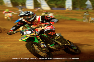 Mehrere Motorradrennfahrer mit Helmen werden während des Rennens eingefangen, mit Text am unteren Bildrand.