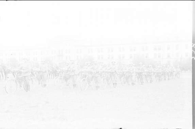 Schwarzes und weißes Foto von Radrennern im Schnee vor einem Gebäude im Hintergrund.