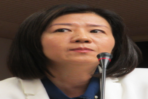 Eine Frau in einem weißen Jackett und Anzug spricht vor einer Wand in ein Mikrofon und hat einen ernsten Gesichtsausdruck.