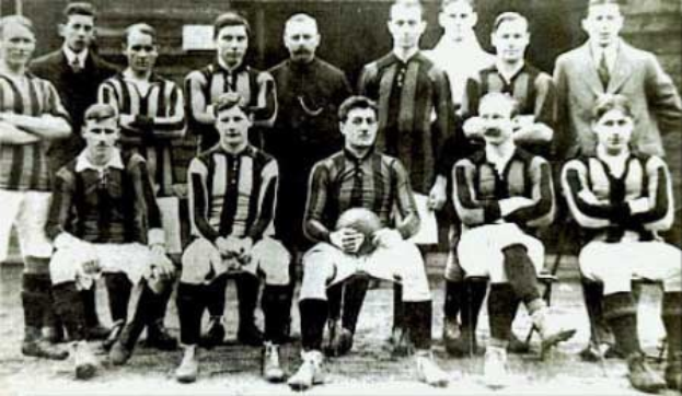 Schwarzes und weißes Foto von Mitgliedern der Fußballmannschaft von Ballymena United, einige stehen und einige sitzen, vor einer Wand.