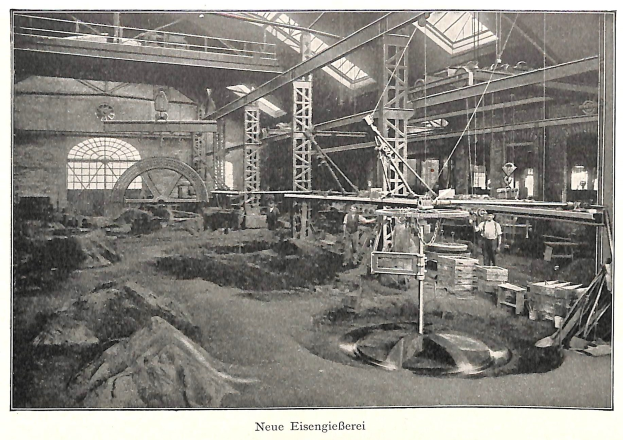 Schwarzes und wei├čes Foto einer Fabrikhalle mit Arbeitern, die an einer Maschine arbeiten, umgeben von Metallstangen und -rohren, beschriftet mit 'Neue Eisenglebeerei, die erste Fabrik in Deutschland' unten.