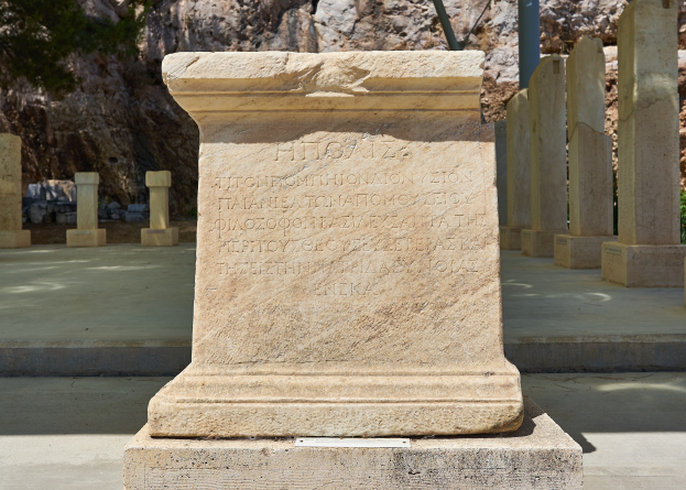Steindenkmal auf einem Friedhof, umgeben von Säulen, Pfosten, Pflanzen, Steinen und Bäumen, mit Inschrift, die wahrscheinlich den Verstorbenen gedenkt.